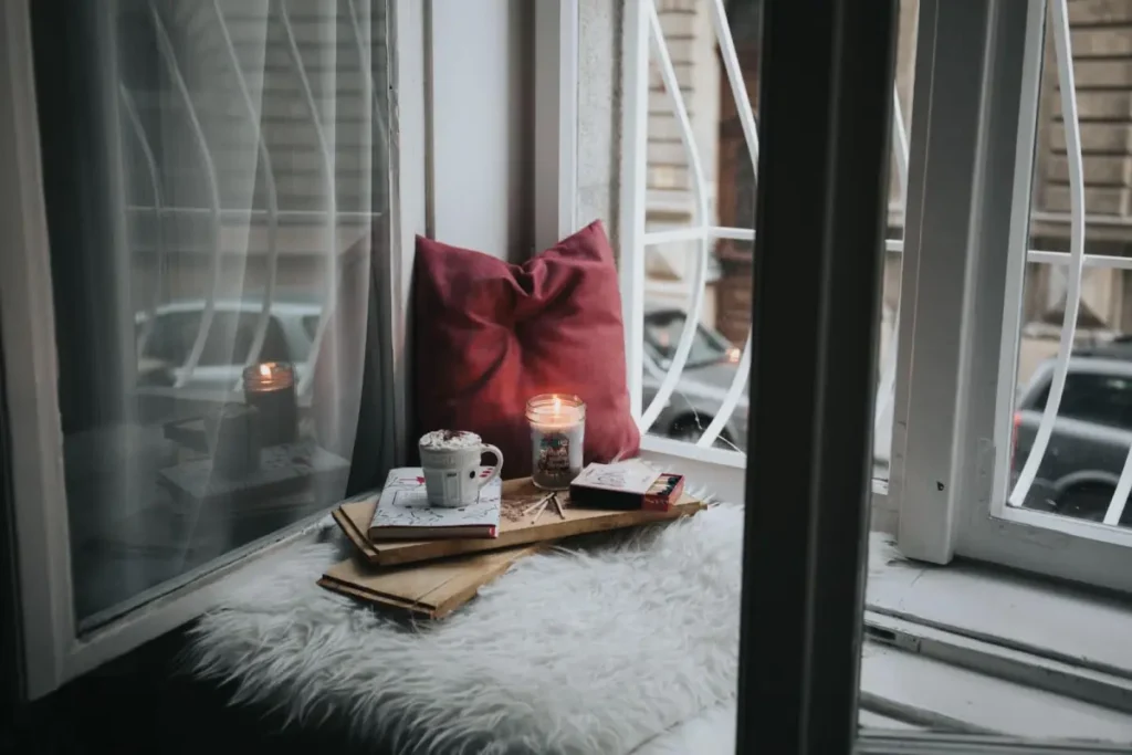 A cozy window nook setup rendered with 3D rendering quality assurance, showcasing pillows and candles.