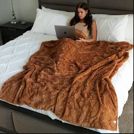 Person relaxing in bed with a laptop and blanket, illustrating cozy lifestyle photography.